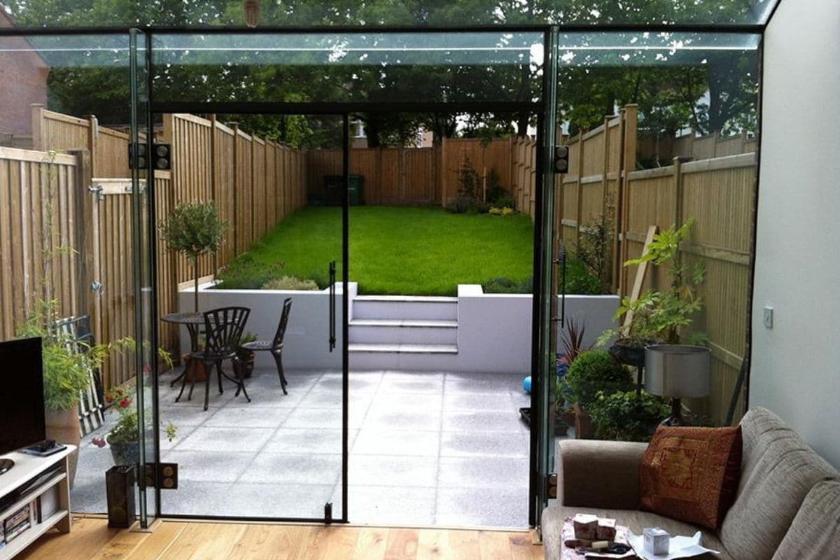 A glass extension extends out the lounge space and merges it with the garden with use of frameless structural glass and double doors