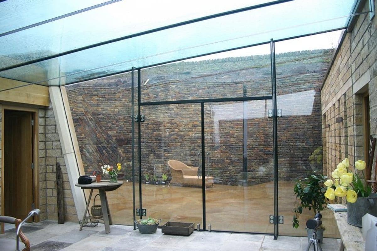 Frameless structural glass encloses this courtyard and links two building together making a practical yet beautiful space