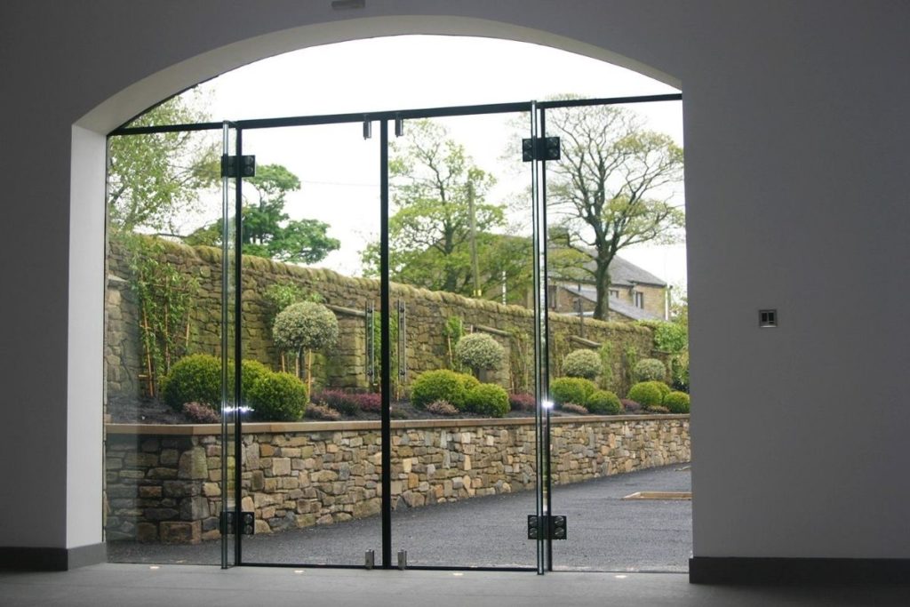 Beautiful oversized frameless glass double doors enclose this large archway opening