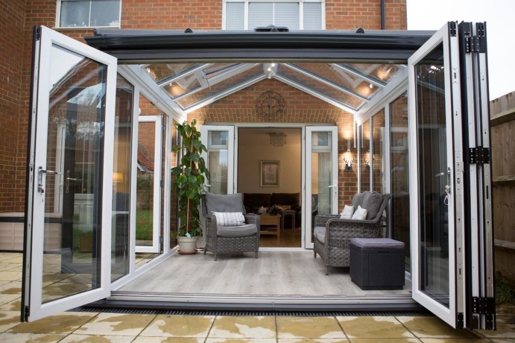 Modern dark grey conservatory exterior and white uPVC inside with bi-fold doors open to the garden