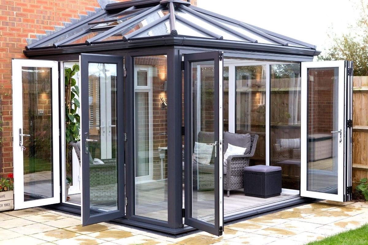 Modern dark grey conservatory exterior and white uPVC inside with bi-fold doors open to the garden