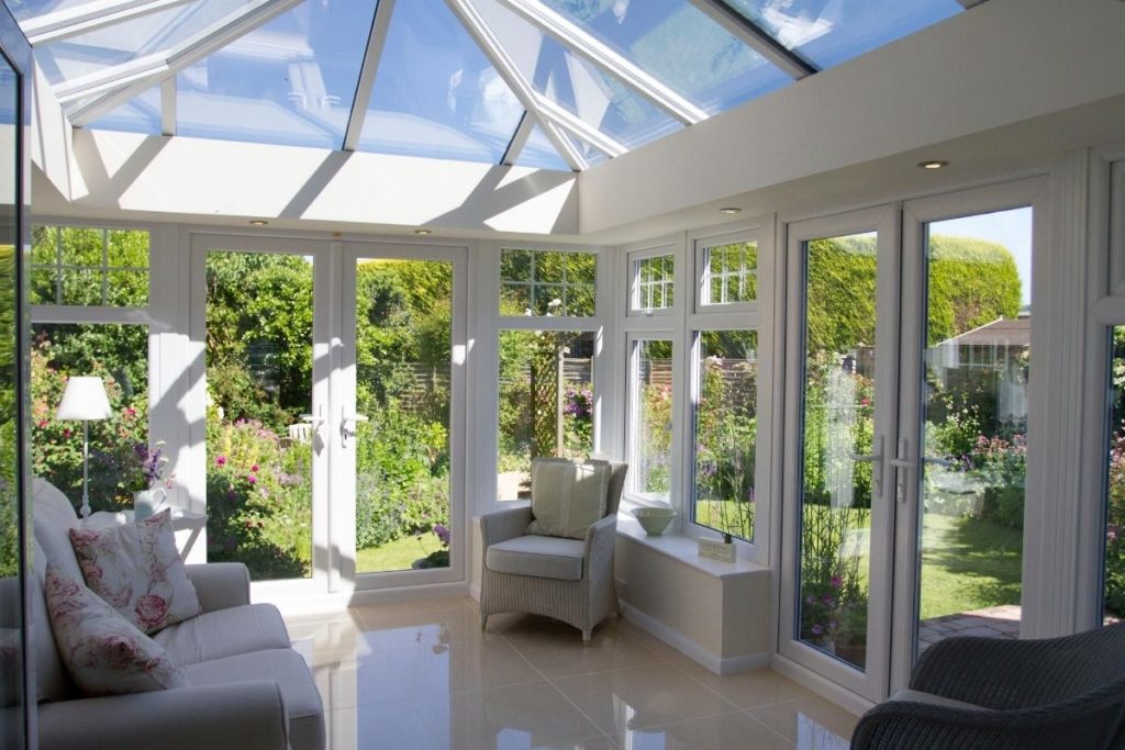 Modern and bright uPVC orangery with full glass lantern roof, double aspect French doors and steps down into a country garden