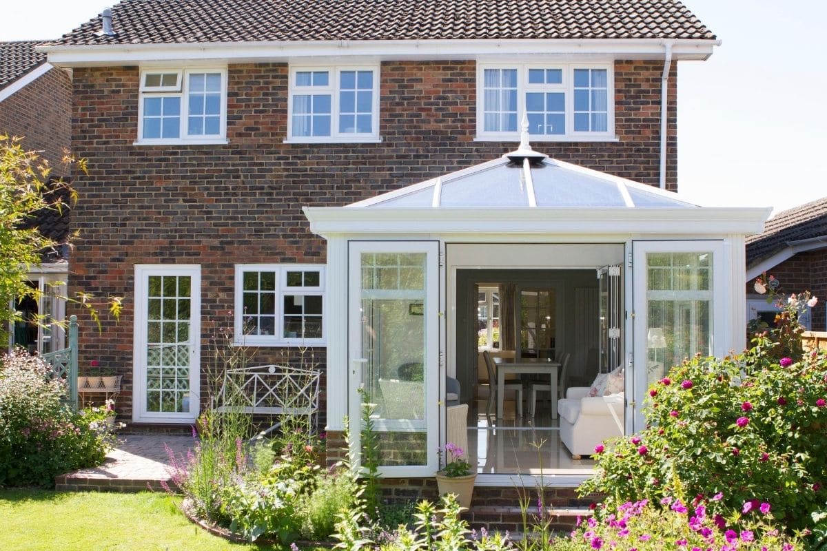 Modern uPVC framed orangery with double doors opening wide to steps down into a Sussex country garden