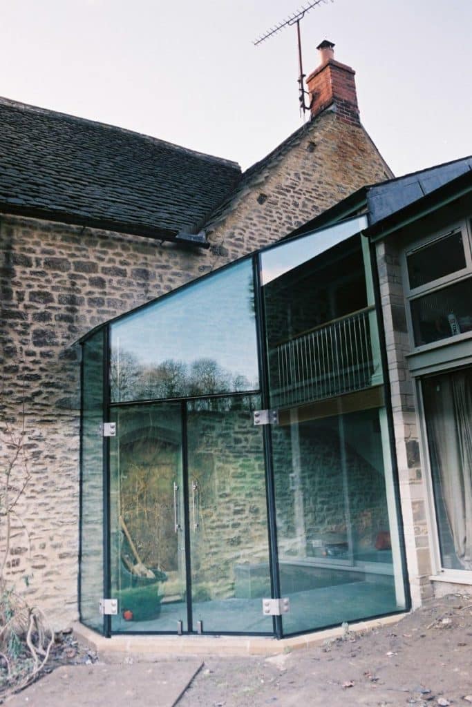 A double storey glass box extension enclosing a patio and balcony