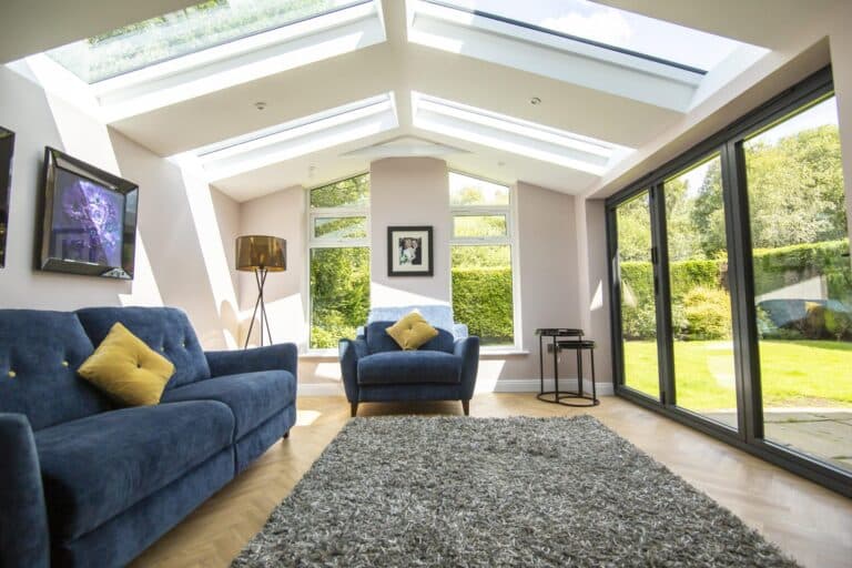 Bright and contemporary modular glass extension with vaulted ceiling, large rooflights, and full-height sliding doors opening to a private garden.
