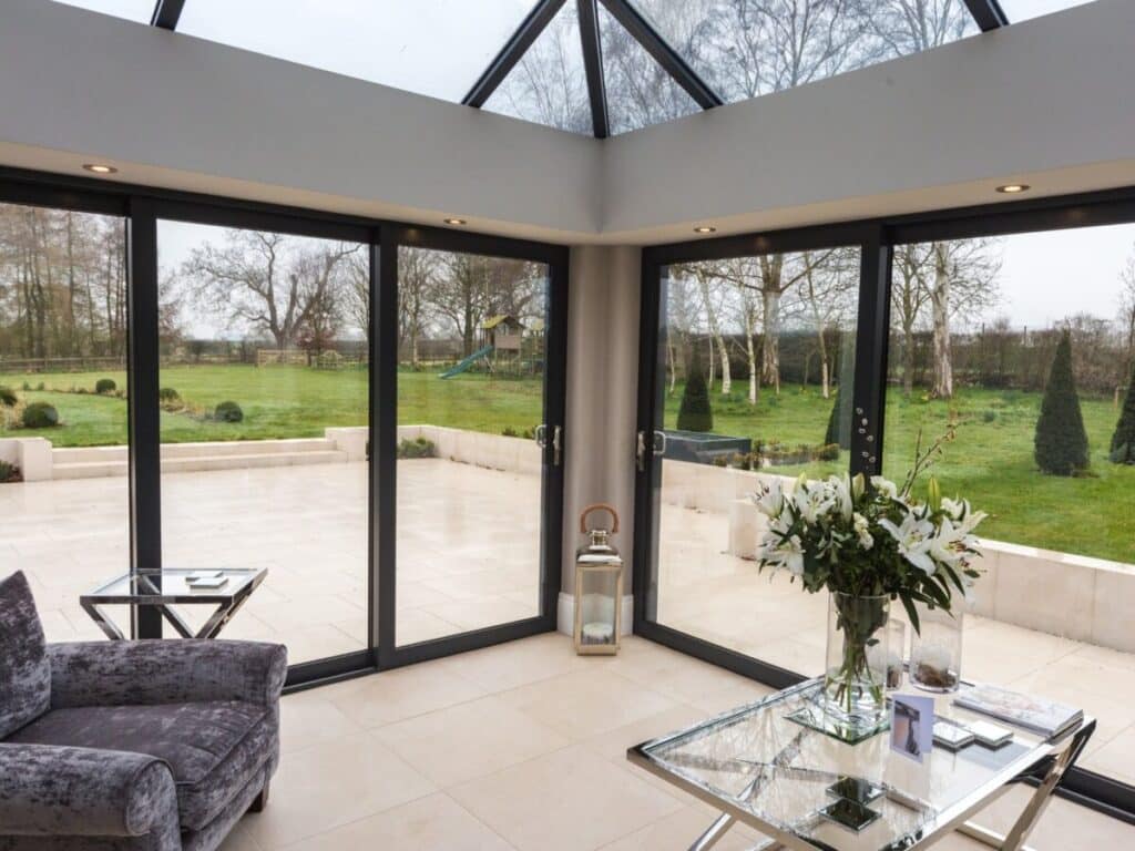 Elegant glass conservatory interior with panoramic garden views and black-framed sliding doors